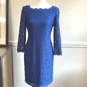 May include: A cobalt blue lace dress with long sleeves and a scalloped neckline. The dress is displayed on a mannequin. The dress is knee-length and has a fitted silhouette.