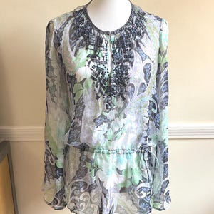 May include: A sheer, long-sleeved blouse with a floral paisley pattern in shades of blue, green, and white. The neckline and upper chest are embellished with dark beading. The blouse has a drawstring waist.