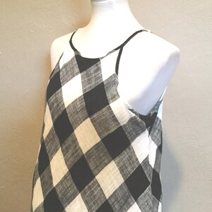 May include: A sleeveless dress with a black and white checkered pattern. The dress has a halter neckline and is displayed on a white mannequin. The fabric appears lightweight and suitable for warm weather.