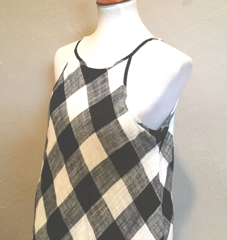 May include: A sleeveless dress with a black and white checkered pattern. The dress has a halter neckline and is displayed on a white mannequin. The fabric appears lightweight and suitable for warm weather.