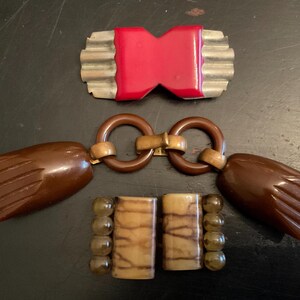 May include: Three vintage plastic belt buckles. One is red and has a silver metal frame. The other two are brown and have a gold metal connector.