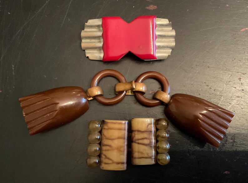 May include: Three vintage plastic belt buckles. One is red and has a silver metal frame. The other two are brown and have a gold metal connector.