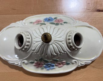 May include: Cream-colored, vintage-style light fixture with two bulb sockets. The fixture is decorated with pink and blue floral accents and a central brass-colored detail. The design features ornate, raised detailing.