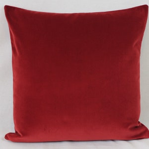 May include: A deep red velvet cushion with a square shape. The cushion is soft and plush, and the fabric has a subtle sheen.