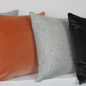 May include: Five decorative throw pillows in various colors and textures. Two pillows are a light gray with a subtle herringbone pattern, one is a dark gray velvet, and two are a burnt orange velvet.