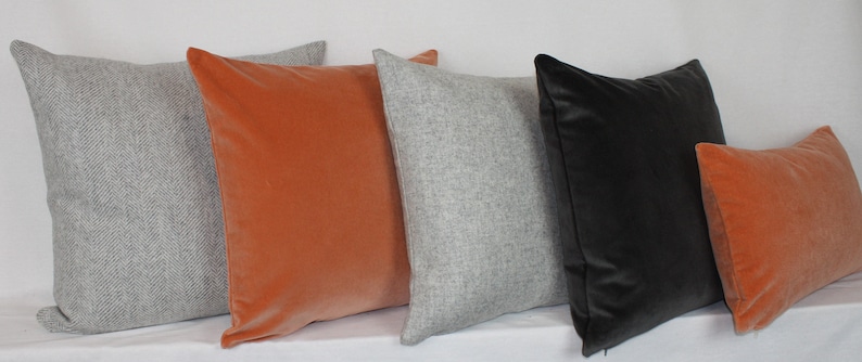 May include: Five decorative throw pillows in various colors and textures. Two pillows are a light gray with a subtle herringbone pattern, one is a dark gray velvet, and two are a burnt orange velvet.