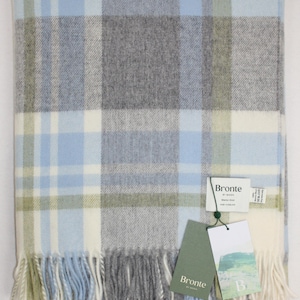 Può includere: Coperta piegata in lana merino Portree Grey e Duck Egg a quadri. La coperta presenta una frangia sul bordo inferiore e un'etichetta Bronte by Moon. La palette di colori include grigio, blu e crema. Realizzata in lana merino.