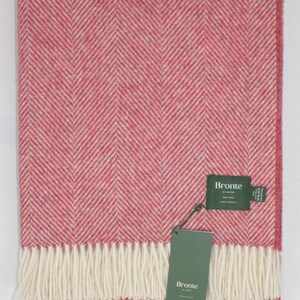 May include: A raspberry herringbone pure wool throw, with a cream fringe. The blanket features a classic herringbone weave pattern in raspberry and cream. The label reads "Bronte by Moon", made in England.