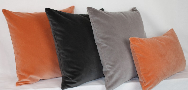 May include: Four decorative throw pillows in various colors. Two are a burnt orange color, one is a dark gray, and one is a light gray.