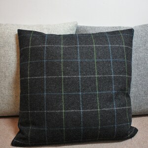 May include: Three square throw pillows. The center pillow is dark gray with a plaid pattern in blue and green. The other two pillows are solid light gray. All pillows have a textured fabric.