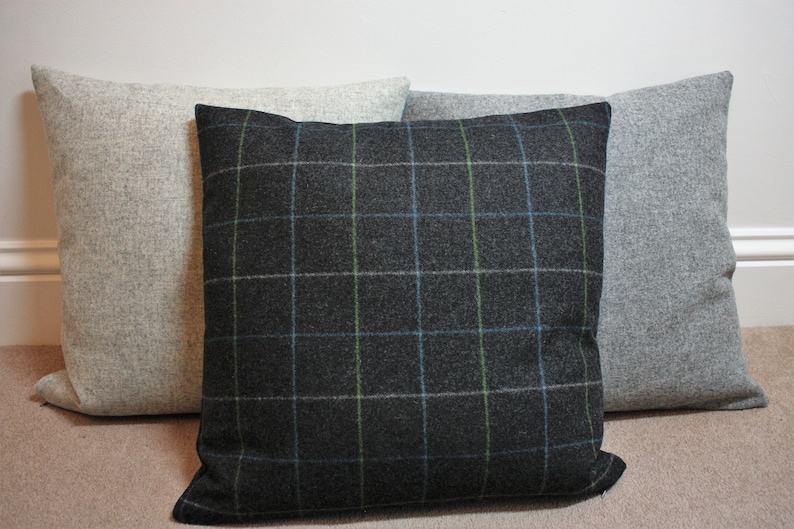 May include: Three square throw pillows. The center pillow is dark gray with a plaid pattern in blue and green. The other two pillows are solid light gray. All pillows have a textured fabric.