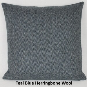 May include: Teal blue square pillow with a herringbone pattern. The pillow is made of wool and has a soft, textured appearance. The text "Teal Blue Herringbone Wool" is printed at the bottom of the image.