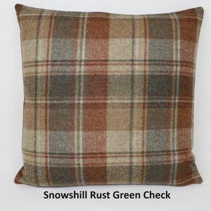 May include: Square cushion featuring a plaid design in brown, rust, green, and beige hues. The cushion has a textured finish, with the text "Snowshill Rust Green Check" printed at the base.