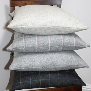 May include: Four square decorative pillows stacked on a wooden chair. The top pillow is a solid light gray, followed by a gray pillow with a pink and white plaid pattern. The third pillow is a solid gray, and the bottom pillow has a dark gray plaid pattern with blue and green accents.