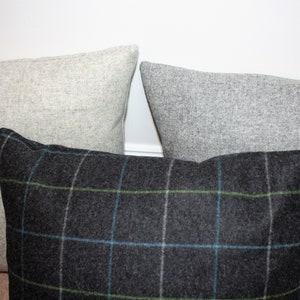 May include: Three decorative throw pillows. Two are solid light gray, and one is dark gray with a plaid pattern in blue and green. The pillows are made of a textured fabric and are arranged in a close-up shot.