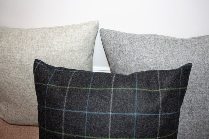 May include: Three decorative throw pillows. Two are solid light gray, and one is dark gray with a plaid pattern in blue and green. The pillows are made of a textured fabric and are arranged in a close-up shot.