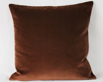 May include: A brown velvet pillow cover. The pillow cover is made of a soft, plush fabric and has a smooth, even texture.
