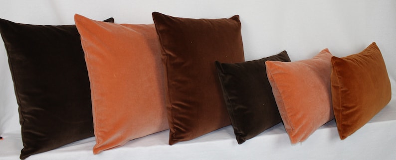 May include: Five decorative throw pillows in a variety of sizes. Two are a burnt orange color and three are a dark brown color.