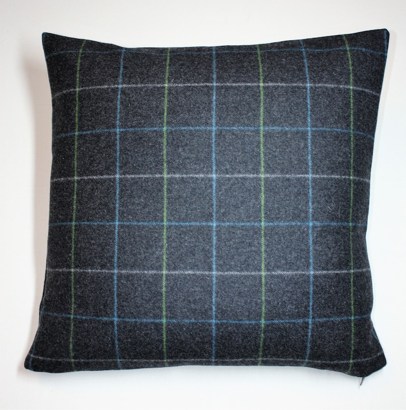 May include: Square decorative pillow with a dark gray plaid pattern. The plaid features a grid of blue, green, and white lines over the gray fabric. The pillow is square and has a soft, textured appearance.