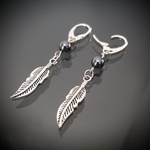 May include: A pair of silver earrings with a black bead and a silver feather charm.