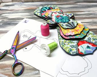 Peut inclure: Plusieurs coussinets en tissu à motifs colorés, avec des motifs floraux et animaliers. Des ciseaux irisés, des bobines de fil rose et vert, et des patrons sont également visibles sur une surface.