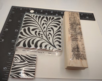 Peut inclure: Trois tampons en caoutchouc sur une surface blanche. Les tampons sont dans un emballage en plastique transparent. Le premier tampon est un motif floral noir et blanc. Le deuxième tampon est un imprimé zèbre noir et blanc. Le troisième tampon est un motif texturé noir et blanc. Les tampons mesurent environ 5 cm sur 5 cm.