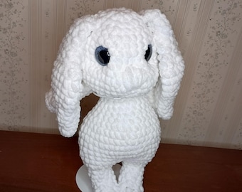 Peut inclure: Un lapin blanc au crochet fait à la main, avec de grands yeux bleu foncé. Le jouet en peluche a de longues oreilles tombantes et repose sur une petite base circulaire blanche. Le lapin est fait de fil doux et texturé.