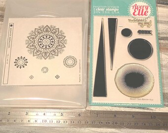 Peut inclure: Deux ensembles de tampons transparents en photopolymère dans des emballages en plastique. Un ensemble présente un grand motif mandala étiqueté Mehndi Medallion. L'autre inclut des formes géométriques et le texte You brighten my day. Une règle métallique affiche une échelle de 27 cm.