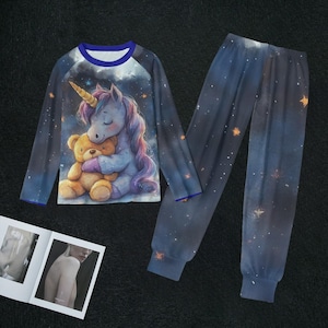 Może przedstawiać: Dwuczęściowy zestaw piżamowy z bluzką z długim rękawem i pasującymi spodniami. Bluzka ma niebiesko-biały wzór z jednorożcem obejmującym misia. Spodnie są granatowe z wzorem gwiaździstego nieba. Piżama ma niebieskie wykończenia.