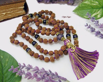 May include: A brown and purple mala with a tassel and an Om symbol charm. The mala is made of Rudraksha beads and amethyst beads.