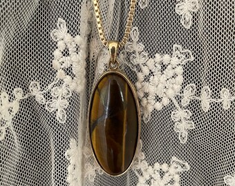 May include: A gold chain necklace with a large oval-shaped tiger's eye pendant.