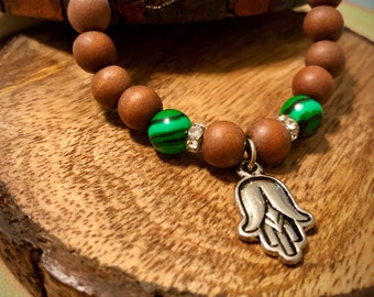 May include: A wooden bracelet with green and white striped beads and a silver hamsa hand charm.