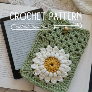 May include: Green crochet phone case with a white daisy flower design. The case is lying on a book with the text "CROCHET PATTERN instant download" visible.