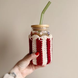 May include: A glass jar with a red and white striped crocheted cozy, a bamboo lid, and a green glass straw.