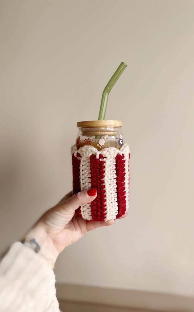 May include: A glass jar with a red and white striped crocheted cozy, a bamboo lid, and a green glass straw.