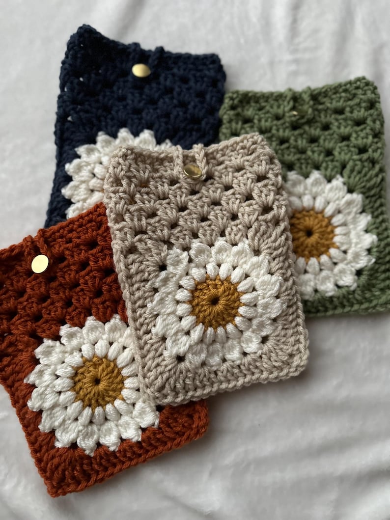 May include: Three crocheted phone cases with a daisy design. The cases are in shades of brown, beige, and green.