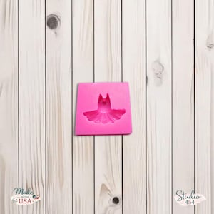 Könnte beinhalten: Eine leuchtend rosa Silikonform in Form eines Balletttutus. Die rechteckige Form hat ein detailliertes Tutu-Design. Der Hintergrund ist ein helles Holzmaserungsmuster. Der Text "Made in the USA" befindet sich unten links.