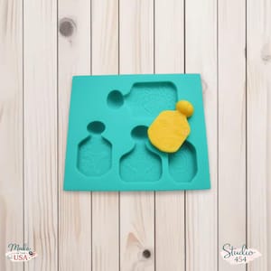 May include: A turquoise silicone mold with four perfume bottle-shaped cavities. One cavity contains a yellow, perfume-shaped piece. The mold has the text "Made in the USA" and "Studio 454".