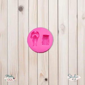 Könnte beinhalten: Eine leuchtend rosa Silikonform mit zwei detaillierten Designs: eine Sandale und ein geflochtener Korb. Die Form ist kreisförmig und liegt auf einer hellen Holzmaserung. Die Worte "Made in the USA" sind unten links sichtbar.