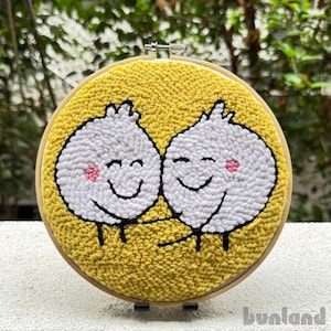 May include: A yellow circular embroidery hoop with two white smiling characters with pink cheeks. The characters are hugging each other. The background is yellow.