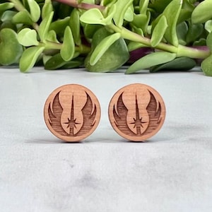 May include: A pair of wooden earrings featuring the Rebel Alliance symbol from Star Wars. The earrings are circular and have a brown wood finish.