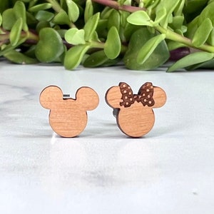 Peut inclure: Une paire de boucles d'oreilles en bois repr&eacute;sentant les personnages de dessin anim&eacute; embl&eacute;matiques Mickey Mouse et Minnie Mouse. Mickey Mouse est repr&eacute;sent&eacute; dans son short rouge classique et ses chaussures jaunes, tandis que Minnie Mouse porte un n&oelig;ud rouge &agrave; pois. Les boucles d'oreilles sont de couleur brun clair et ont un design simple et minimaliste.