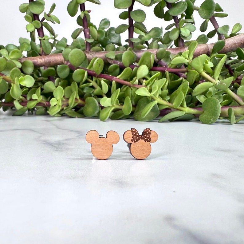 Peut inclure: Une paire de boucles d'oreilles en bois repr&eacute;sentant les personnages de dessin anim&eacute; embl&eacute;matiques Mickey Mouse et Minnie Mouse. Mickey Mouse est repr&eacute;sent&eacute; dans son short rouge classique et ses chaussures jaunes, tandis que Minnie Mouse porte un n&oelig;ud rouge &agrave; pois. Les boucles d'oreilles sont de couleur brun clair et ont un design simple et minimaliste.