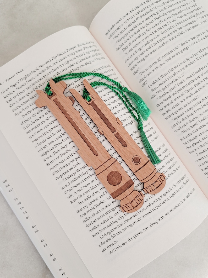 May include: Three wooden bookmarks with green tassels. Each bookmark features a unique design of a spaceship, a rocket, and a satellite. The bookmarks are ideal for book lovers and space enthusiasts.