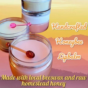 May include: Three jars of handcrafted honeybee lip balm. The lip balm is made with local beeswax and raw homestead honey. The jars are clear and show the lip balm inside. The lip balm is a light pink color. The jars are on a background of a sunset.