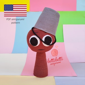 May include: A handmade, red amigurumi figure with large white and black eyes, wearing a gray hat and black glasses. The figure has a long, cylindrical body. The image includes the text "PDF amigurumi pattern" and the American flag.