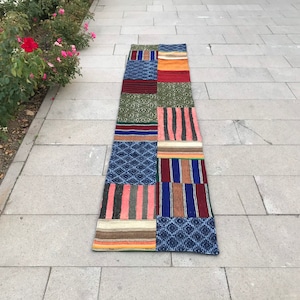 May include: A long, narrow patchwork rug with a variety of colors and patterns, including red, blue, green, and brown. The rug is made of different fabrics sewn together.