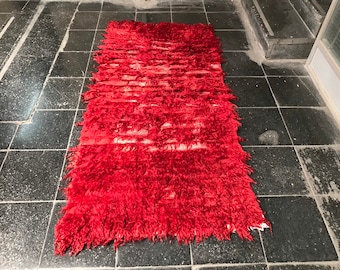 May include: A red shag rug with a white stripe pattern. The rug is made of a soft, fluffy material and has a long fringe.