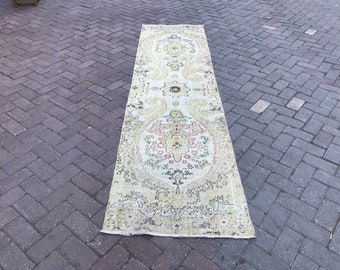 May include: A long, off-white runner rug with a floral pattern in shades of pink, green, and brown. The rug has a distressed, vintage look.