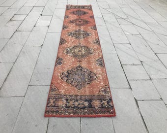 Peut inclure: Un tapis long et rectangulaire avec un motif persan traditionnel. Le tapis a un aspect délavé et vieilli et présente une palette de couleurs rouge, orange et noire.